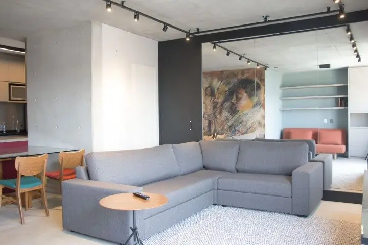 Sala integrada com sofá em L cinza e mesa de jantar atrás Projeto e Monica Spada Durante