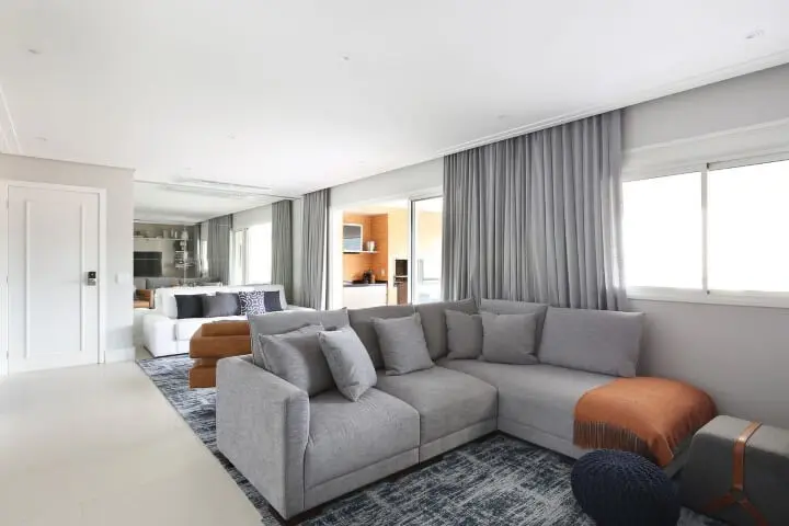 Sala integrada com sofá em L cinza e tapete mesclado em todo o espaço Projeto de Esther Zanquetta