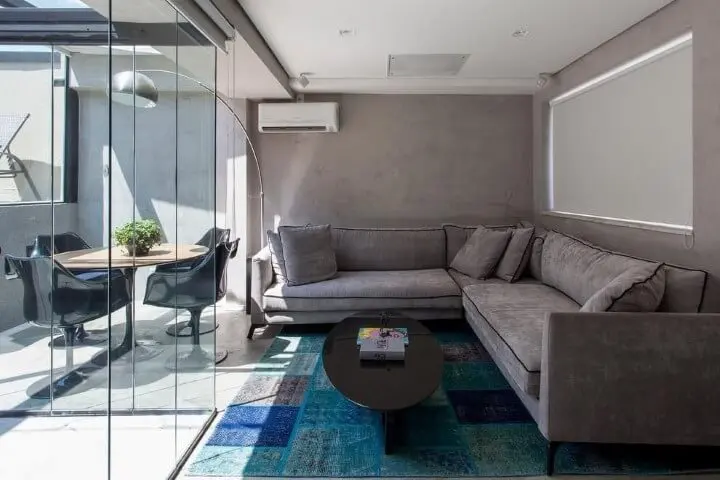 Sala integrada à varanda com sofá em L cinza e mesa de centro preto Projeto de Tria Arquitetura