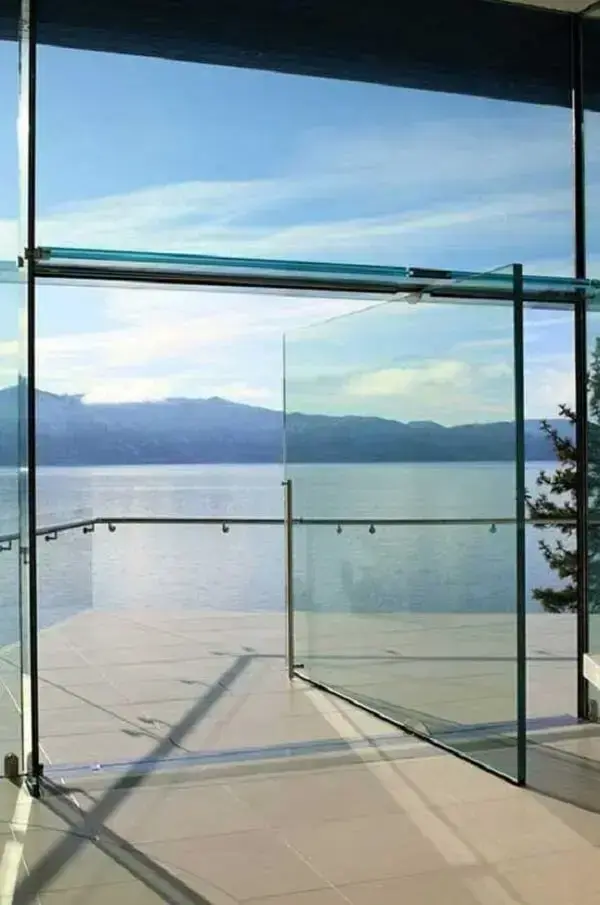 A porta pivotante de vidro se mistura com a paisagem externa do imóvel