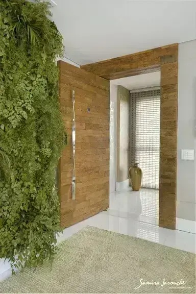 Hall com plantas na parede e porta pivotante madeira de demolição e puxador em formato torcido Projeto de Samira Jarouche