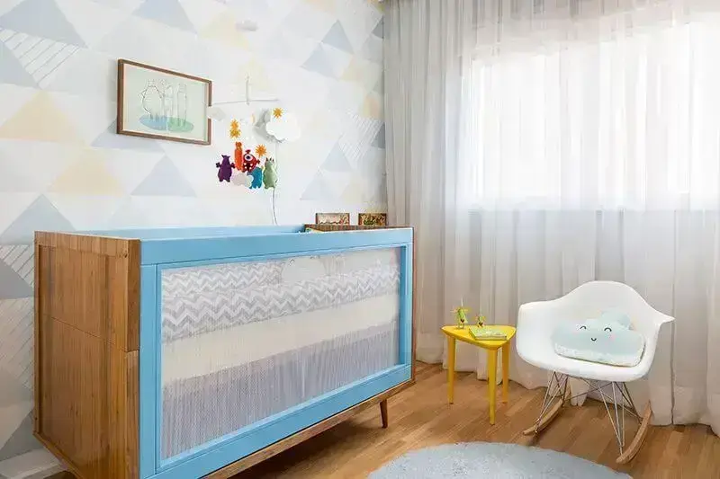 Quarto de bebê menino com berço de madeira com laterais azuis e papel de parede com triângulos Projeto de Studio Novak