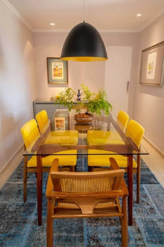 pendente sala de jantar pequena decorada com tapete azul cadeiras amarelas e mesa de vidro Foto Apê Vinte Dois