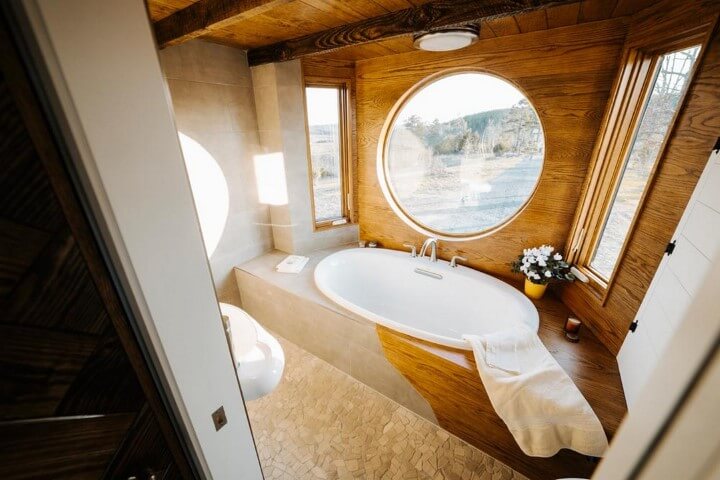 Banheira pequena com formato ovalado em banheiro com revestimento de pedra e madeira Foto de Possible Decor