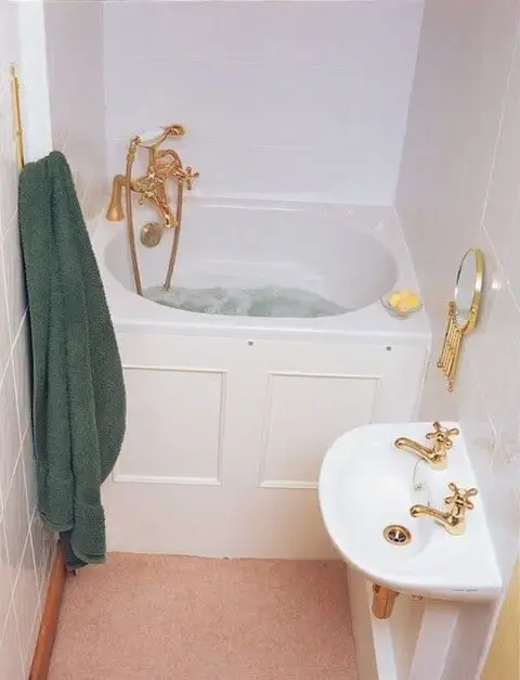 Banheira pequena com torneiras douradas combinando com a decoração do banheiro Foto de Boblewislaw