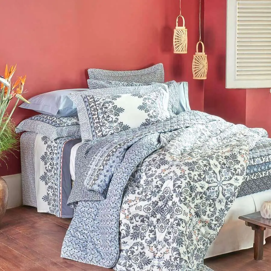 quarto decorado com parede goiaba e cama com muitos travesseiros e lençóis azuis