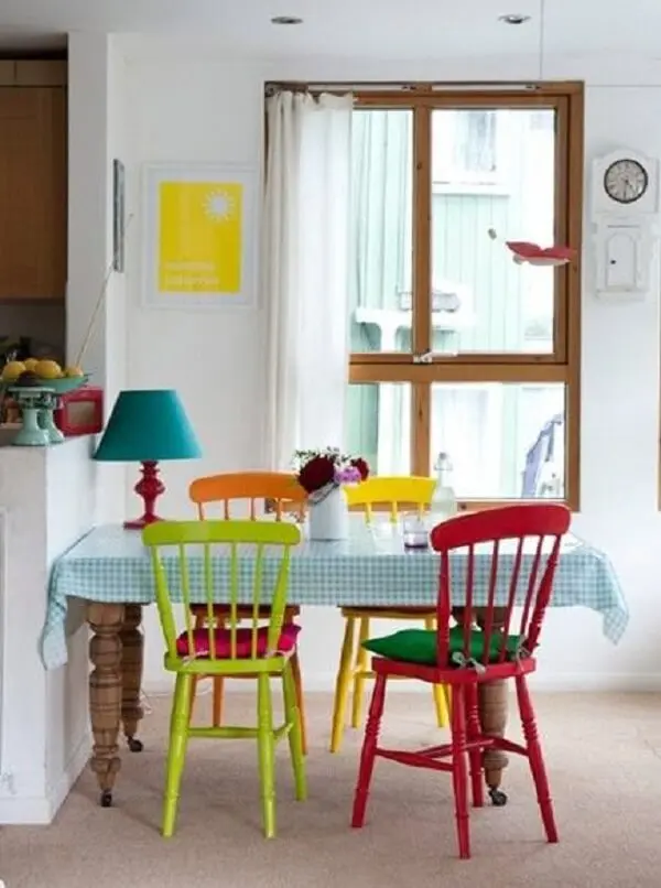 Decoração de sala simples e barata tem mesa branca com cadeiras coloridas 