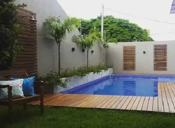 Área de lazer pequena com piscina em deck de madeira interligando ambientes