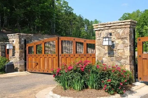 Entrada de chácara composta por um portão de madeira e canteiro de flores