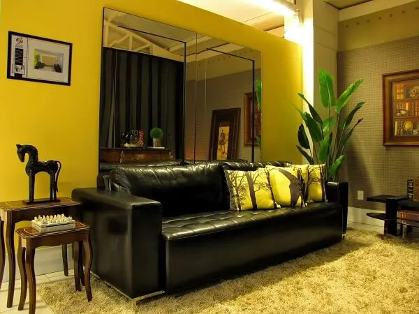 O sofá de couro preto equilibra o ambiente da sala com parede na cor amarela