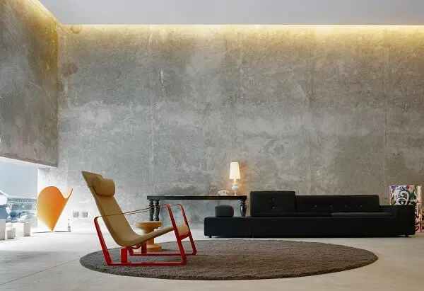 Paredes na cor concreto, sofá preto e tapete marrom complementam a decoração