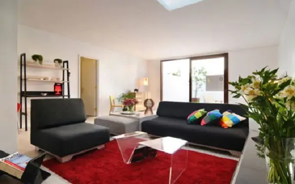 Sofá preto e tapete vermelho complementam a decoração do ambiente