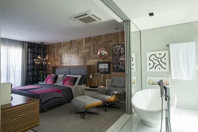 quarto de casal moderno - cama ao lado de poltrona cinza e banheiro com banheira e parede de espelhos