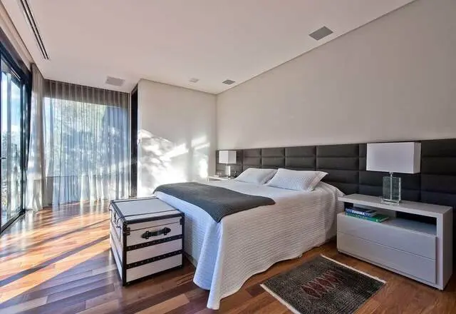 quarto de casal moderno - cama atrás de baú branco e preto e em frente a painel estofado
