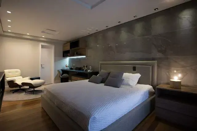 quarto de casal moderno - cama centralizada, ao lado de poltrona branca e em frente à parede cinza