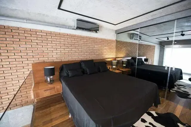 quarto de casal moderno - cama centralizada com lençois pretos ao lafo e parede de espelhos e em frente a parede de tijolos