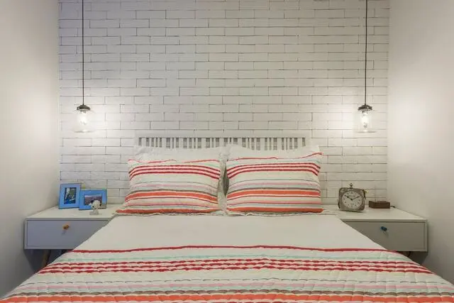 quarto de casal moderno - cama centralizada, em frente a parede de tijolos brancos com duas luminárias de teto