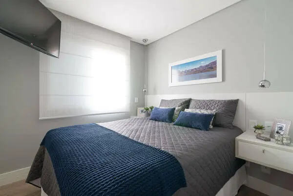 quarto de casal moderno - cama com lençois azul e cinza em frente de tv afixada na parede