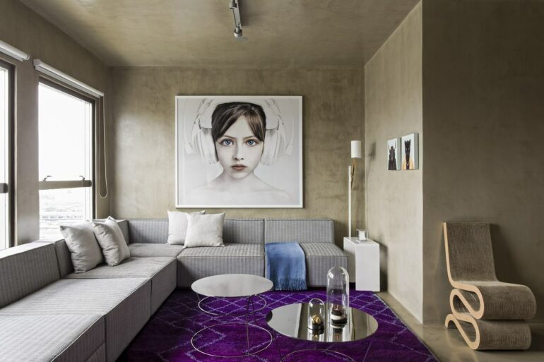 Decoração moderna para sala com parede de cimento queimado, sofá de canto e grande quadro tumblr – Foto Archello