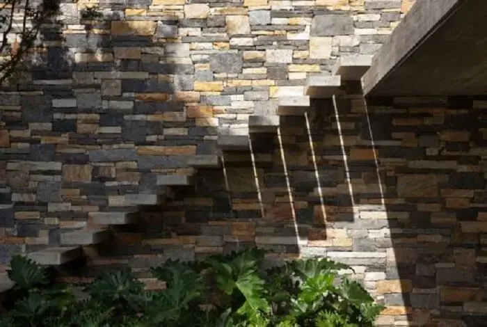 Escada flutuante de concreto da área externa fixada na parede de pedra