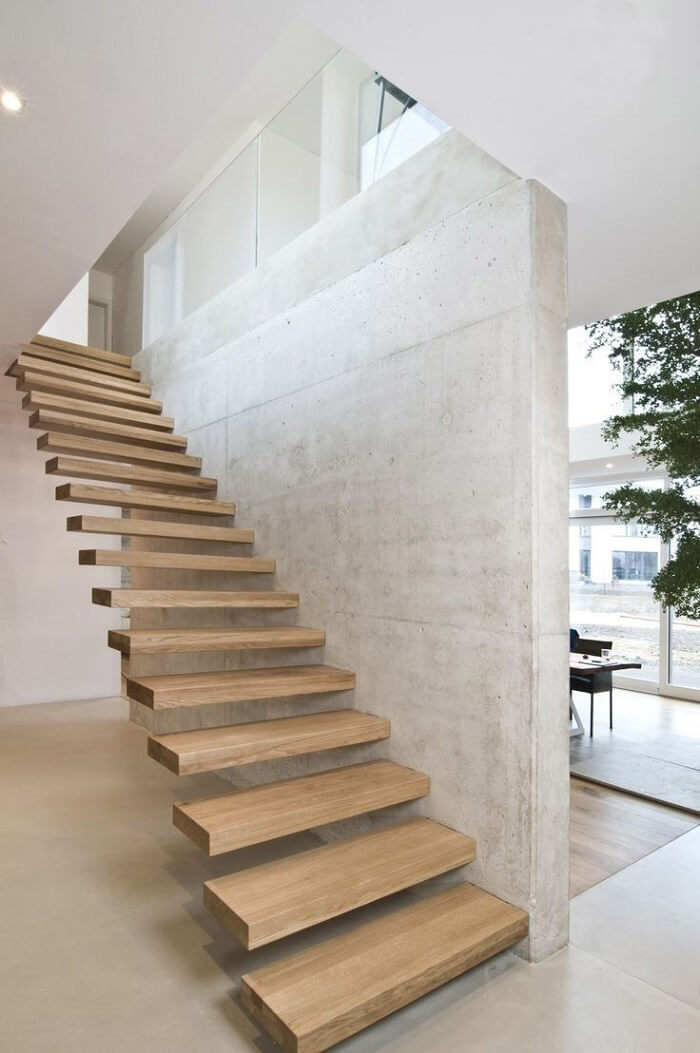 Escada flutuante de madeira clara fixada em parede de concreto