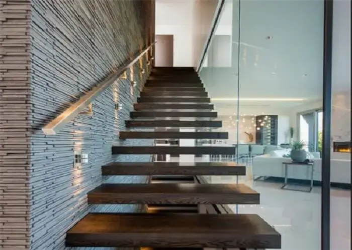 Escada flutuante de madeira com lateral envidraçada e pontos de iluminação na parede