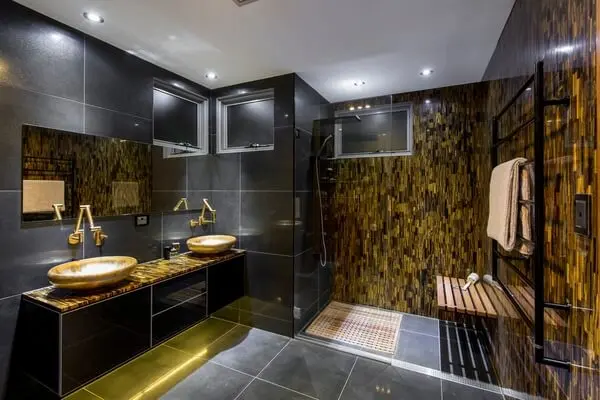 O dourado presente no revestimento da parede e no armário do banheiro encanta a decoração