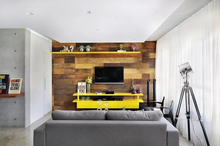 decoração sala de estar com rack amarelo e parede com revestimento de madeira