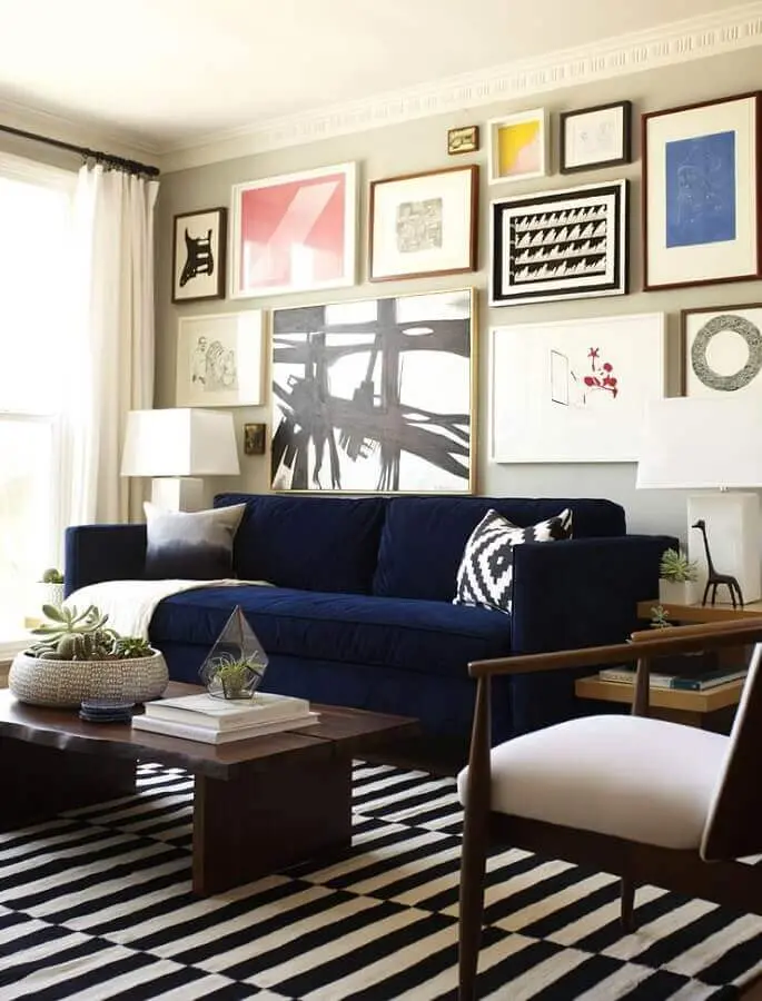 sofá azul escuro para sala decorada com tapete preto e branco e vários quadros Foto PopSugar