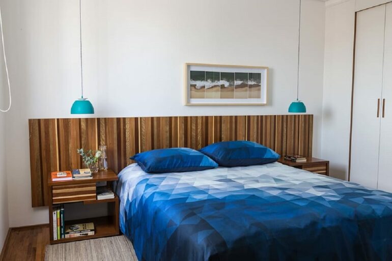 Decoração simples com luminária pendente para quarto de casal azul e branco com cabeceira de madeira. Projeto de Estúdio Paulo Alves