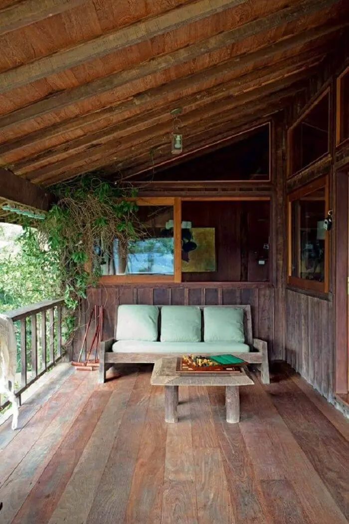 O sofá de três lugares com tecido verde complementa a decoração da varanda de madeira