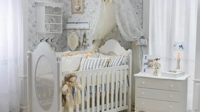 Quarto de bebê com berço provençal branco e papel de parede floral azul