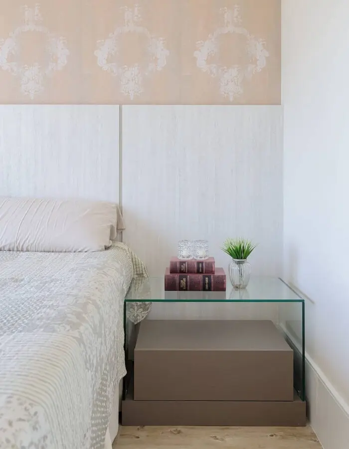 Papel de parede, cabeceira de madeira branca e criado mudo com vidro encanta a decoração deste quarto
