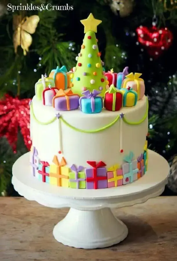 bolo de natal decorado com pasta americana com caixinhas de presentes coloridas e pequena árvore de natal no topo Foto Sprinkles & Crumbs