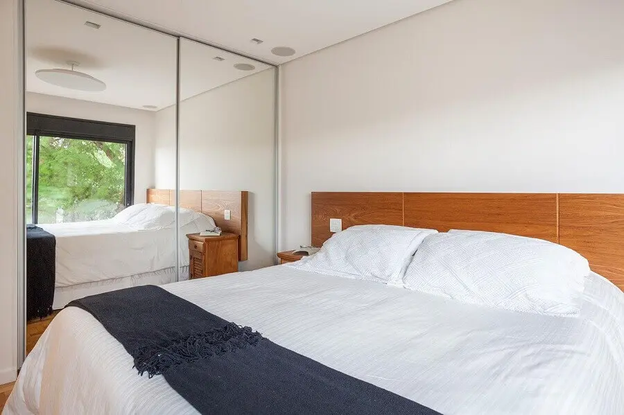 decoração clean para quarto de casal com cabeceira de madeira e guarda roupa com espelho Foto Tria Arquitetura