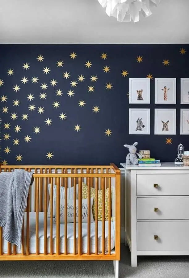 quarto de bebê azul marinho com berço de madeira e estrelinhas douradas na parede Foto Ideias Decor