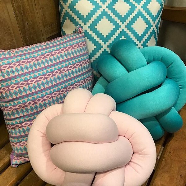 Almofada do tipo nó em tom rosa claro e azul turquesa decoram o ambiente