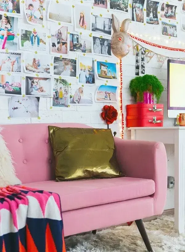Decoração colorida composta por sofá rosa, almofada dourada e painel de fotos na parede