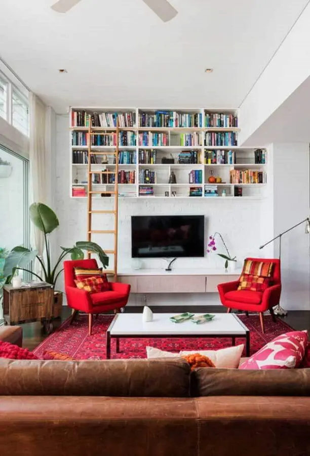 poltrona vermelha para sala decorada com sofá de couro e nichos para livros Foto Jeito de Casa