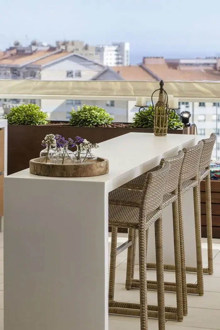 As banquetas de fibra sintética e bancada branca são móveis para varanda perfeitos.