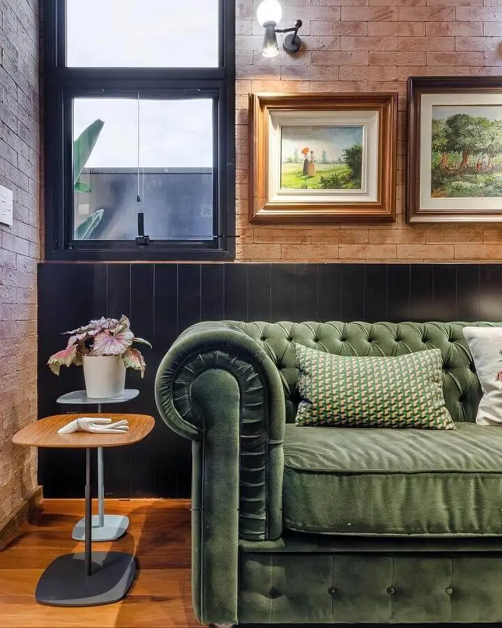 sala decorada com parede de tijolinho e sofá verde com acabamento capitonê Foto Andrea Murão