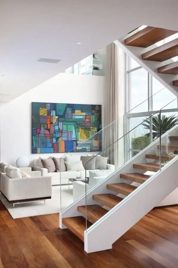 A escada de madeira com vidro se integra perfeitamente com a decoração da sala de estar