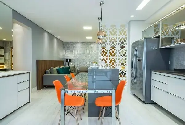 Mesa de jantar de vidro, cadeiras laranjas e armários brancos
