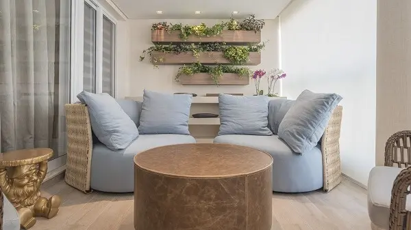 Varanda com sofá em tons neutros, mesa de canto dourada e floreira de madeira