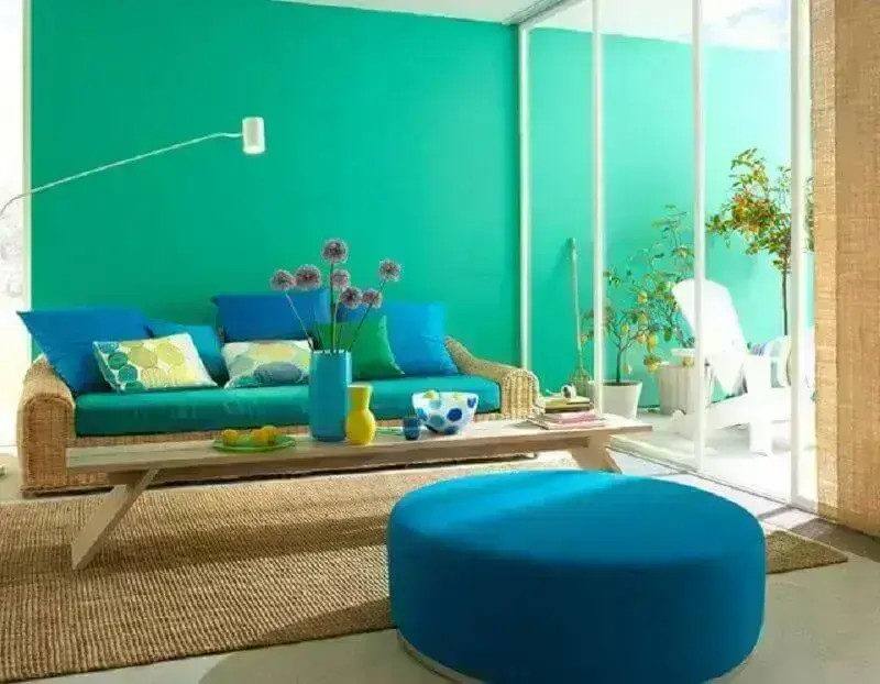 Sala de estar com parede verde água, sofá de vime e puff redondo azul- Foto: Jaeger Arquitetura