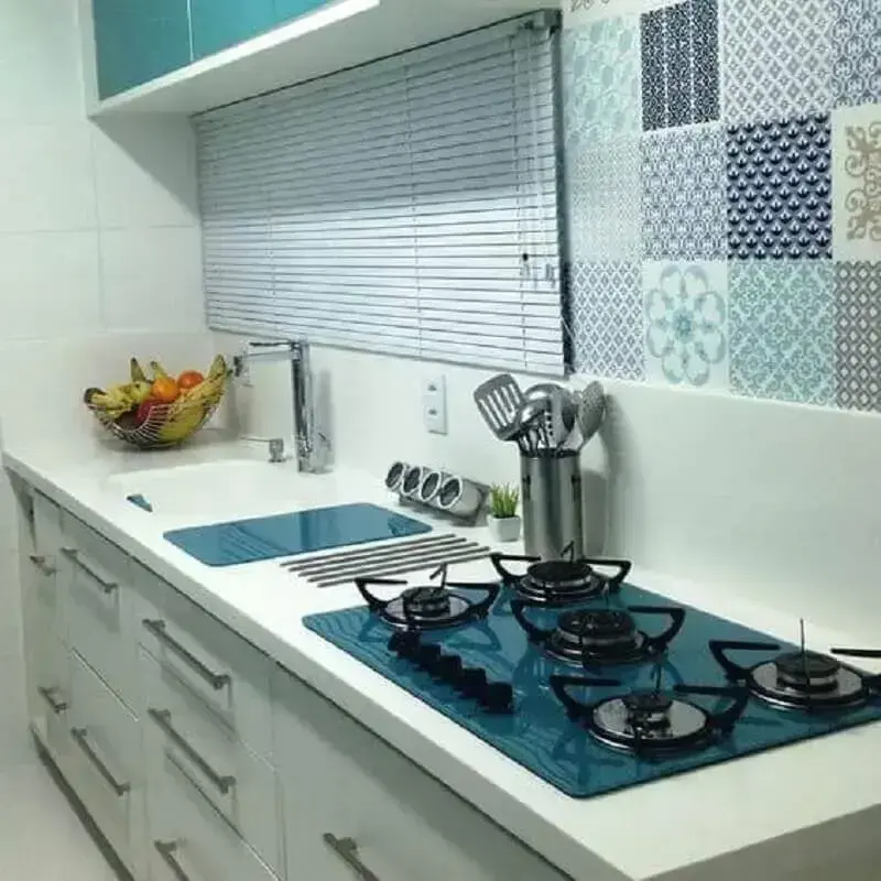 Cozinha colorida com armários em tom de azul petróleo e cooktop na bancada de granito preto