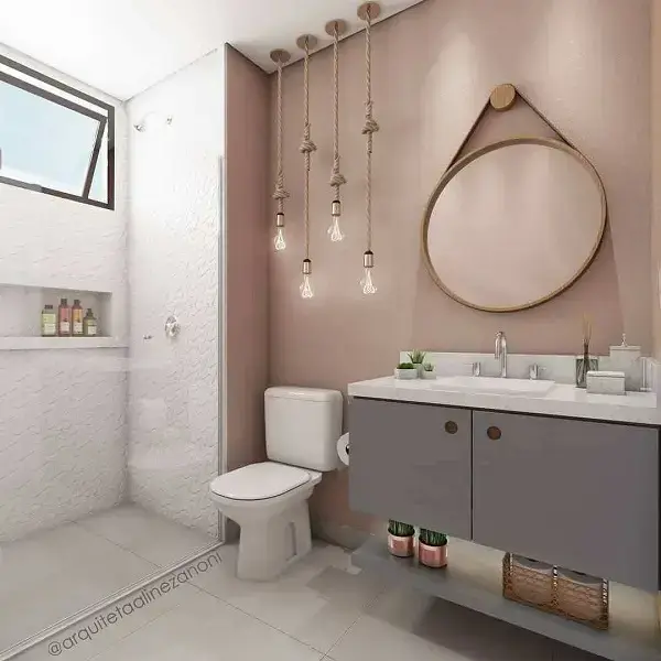 Banheiro rose gold com gabinete cinza espelho redondo e luminárias pendentes