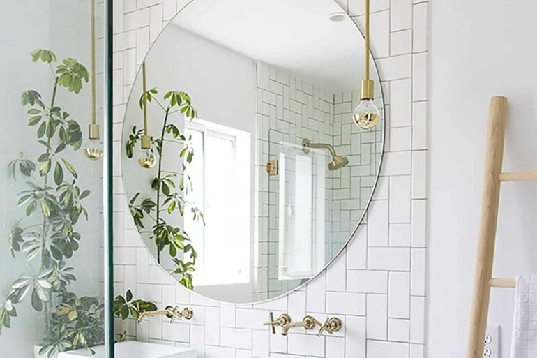 Decoração clean com espelho para banheiro redondo e gabinete suspenso de madeira. Foto: PURE Design Inc