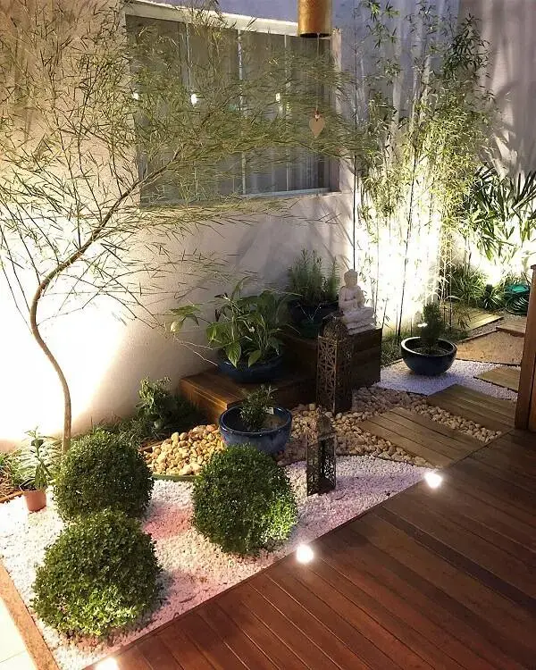 Jardim de inverno com canteiros de pedras brancas, diferentes plantas e iluminação