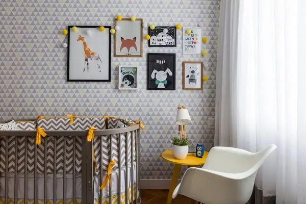 Quarto de bebê cinza e amarelo com mesa de centro amarela e parede estampada